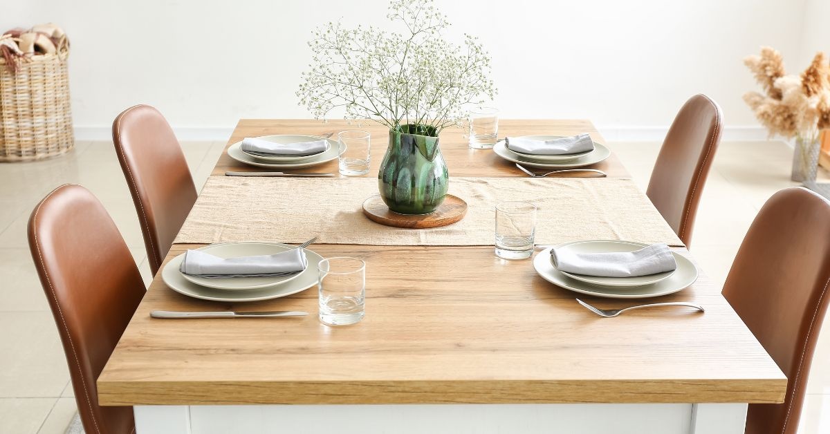 A wooden table with 4 brown chairs around and dishes on top of the table