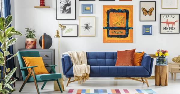 In a colorful room, there is a foldable chair on the left and blue sofa in the middle. Many paintings on the wall